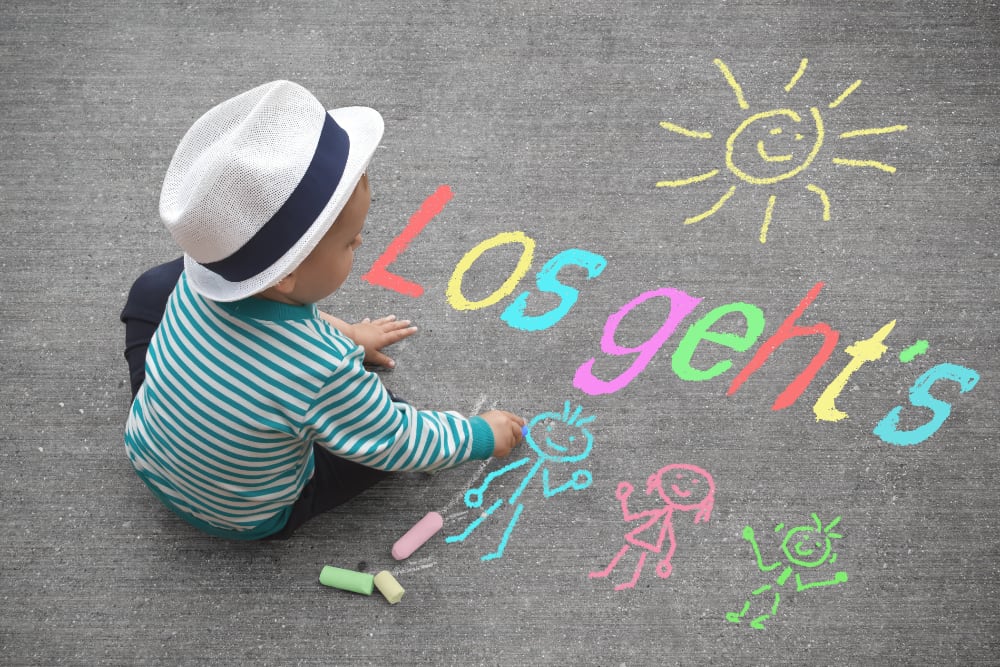 Ein Kind malt Figuren auf den Boden, darüber steht "Los geht's"